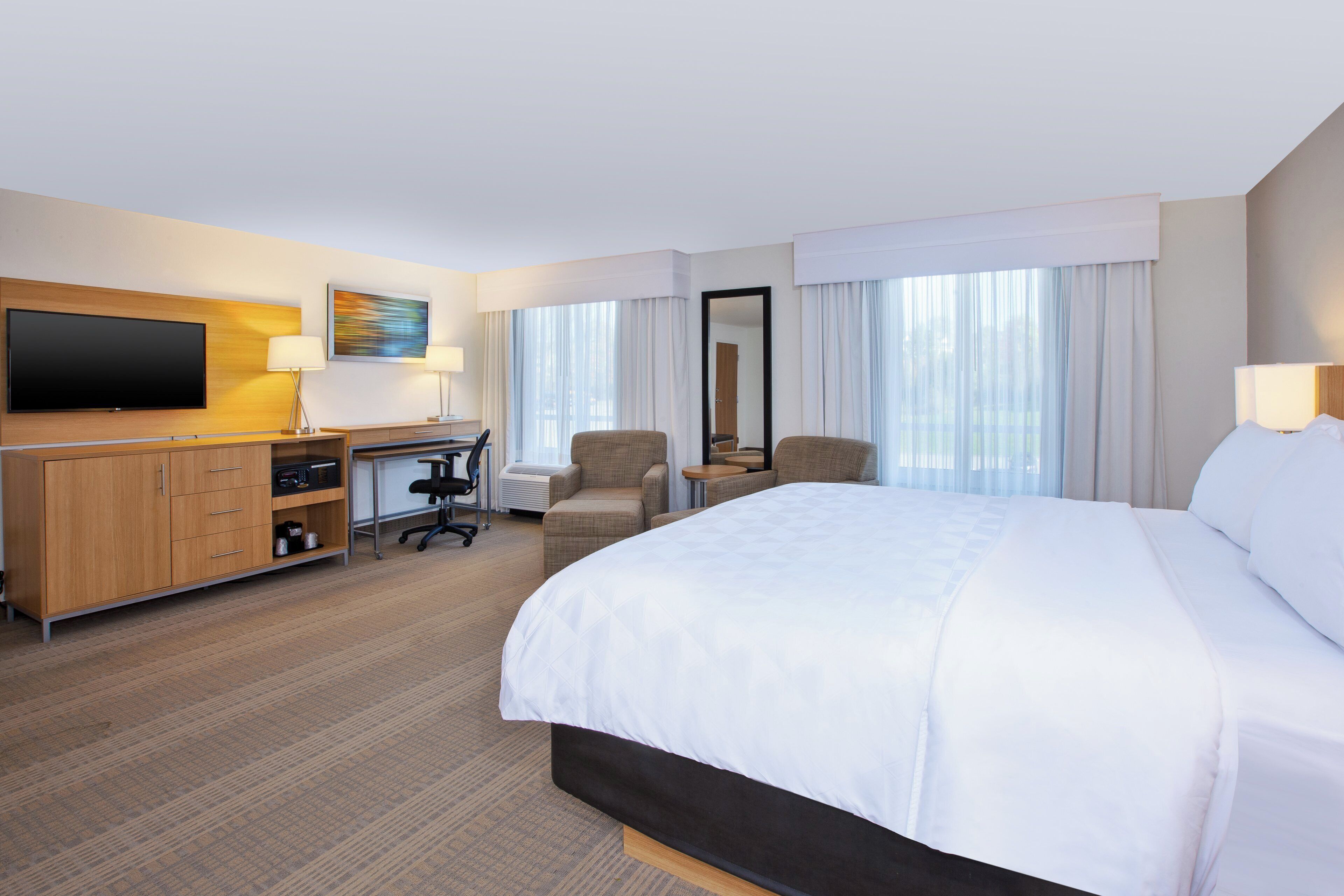A hotel room with a large bed, a desk with a computer, a TV, and a chair.