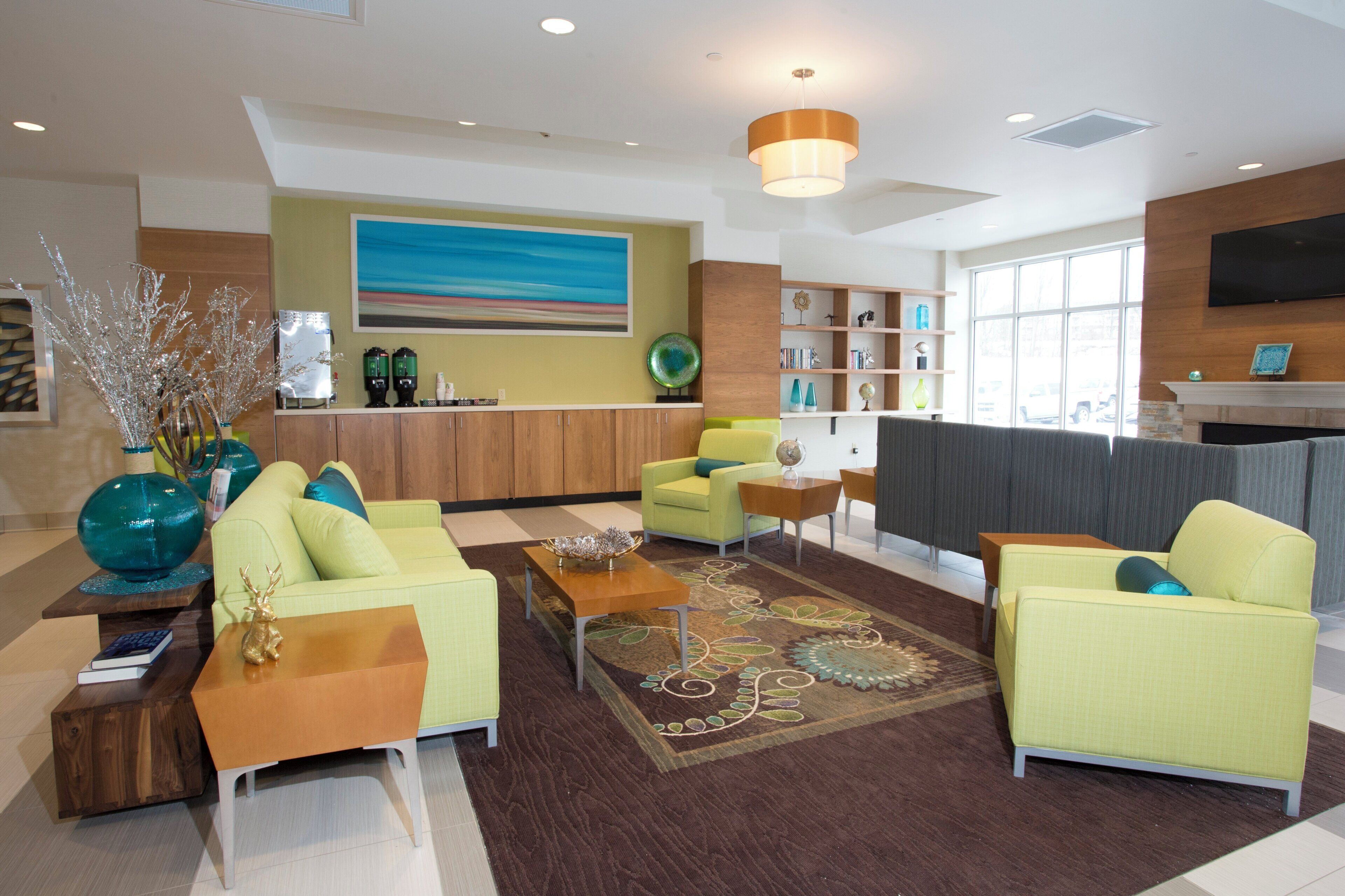 A hotel lobby with a reception desk, seating area with sofas and armchairs, a coffee table, decorative vases, and a large painting on the wall.