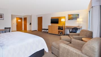 A hotel room with a large bed, a desk with a computer, a TV, and two armchairs.