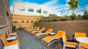 A patio area with orange chairs and tables, a brick wall, and a building in the background.