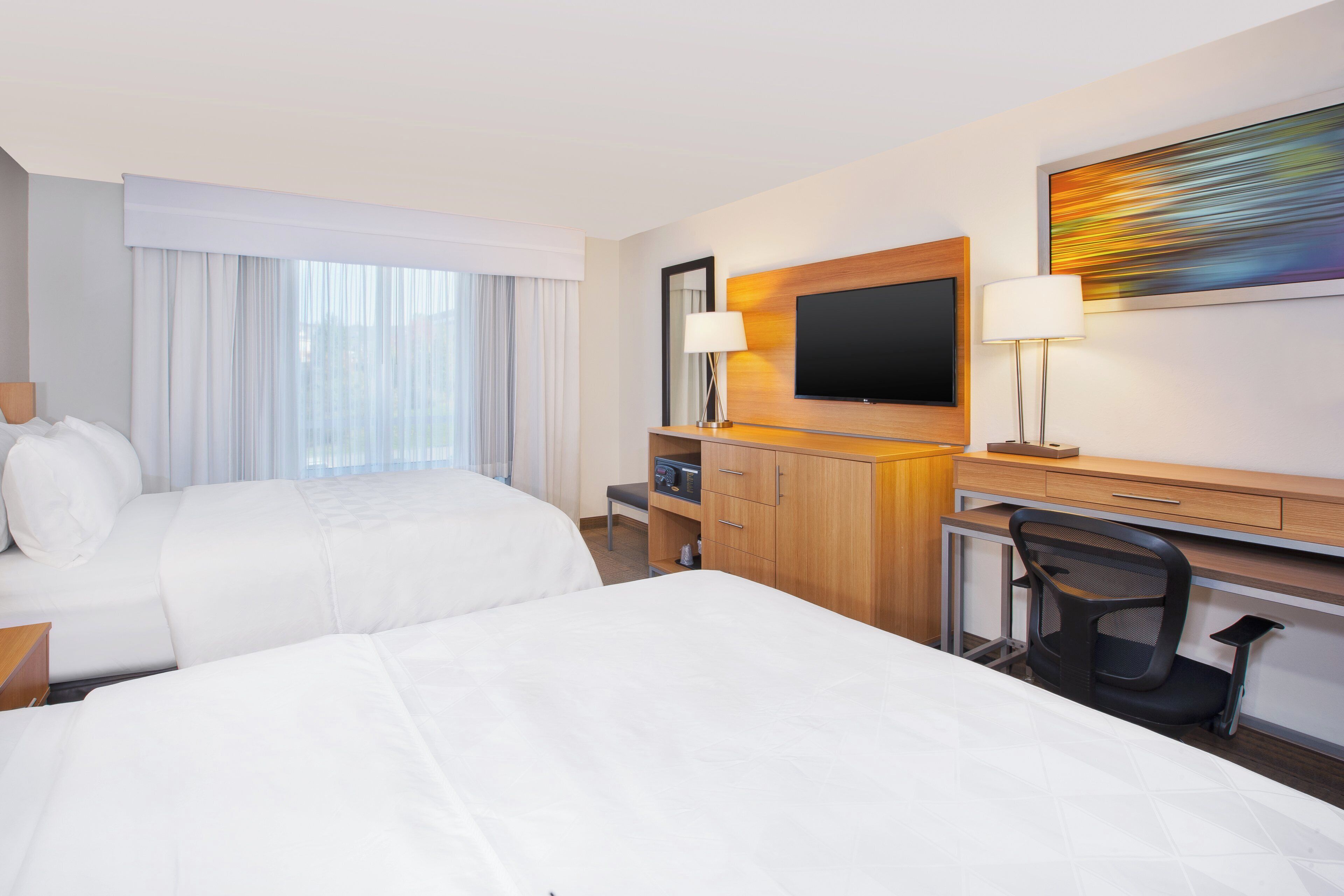 A hotel room with two beds, a desk with a chair, a TV, and a painting on the wall.