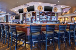A bar area with a wooden counter, multiple stools, and a variety of bottles and glasses.