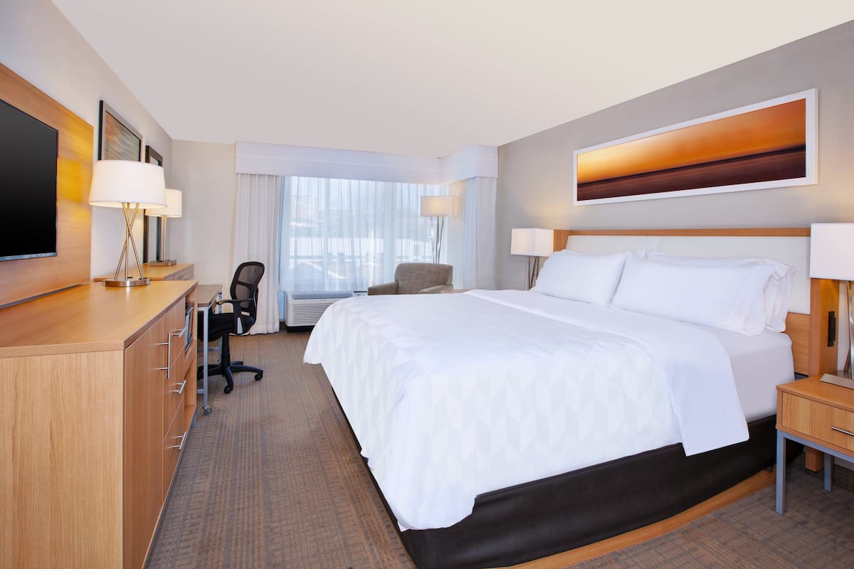 A hotel room with a large bed, a desk with a chair, a television, and a window with curtains.