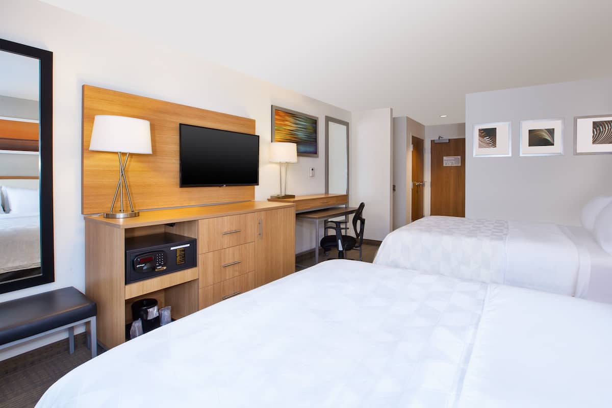 A hotel room with two beds, a desk with a computer, a TV, and a coffee machine.