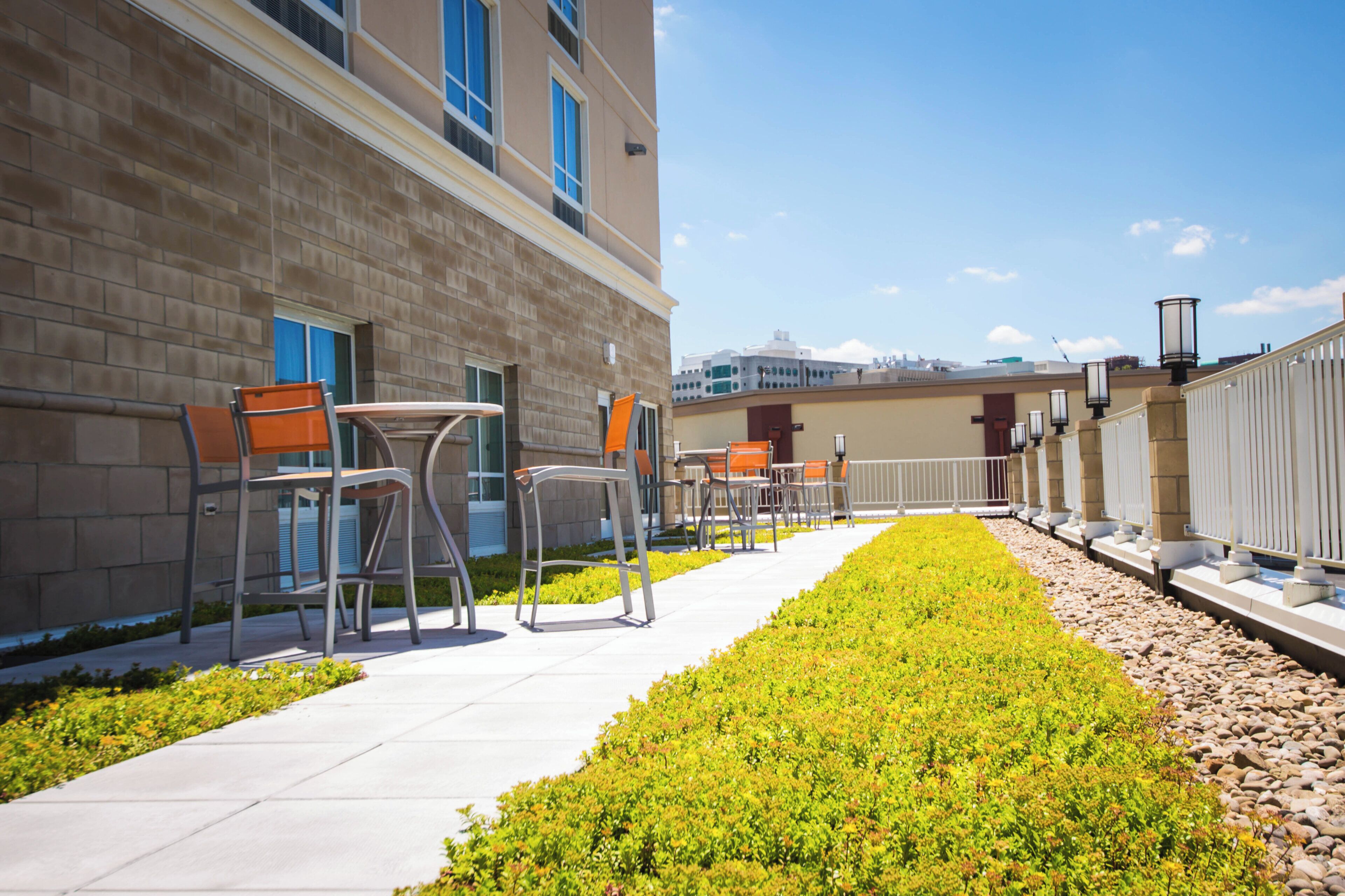 An outdoor seating area with tables and chairs, a pathway, and a building in the background.