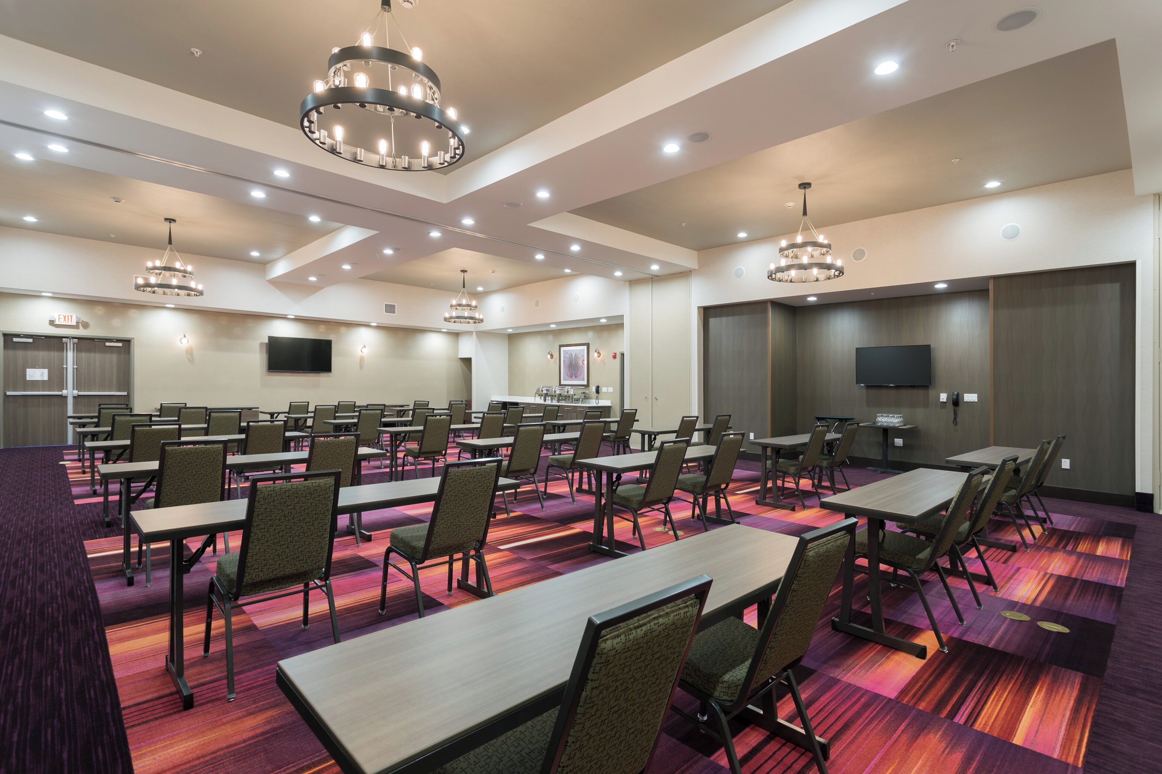 A conference room with multiple tables and chairs, equipped with ceiling lights and a flat-screen TV.