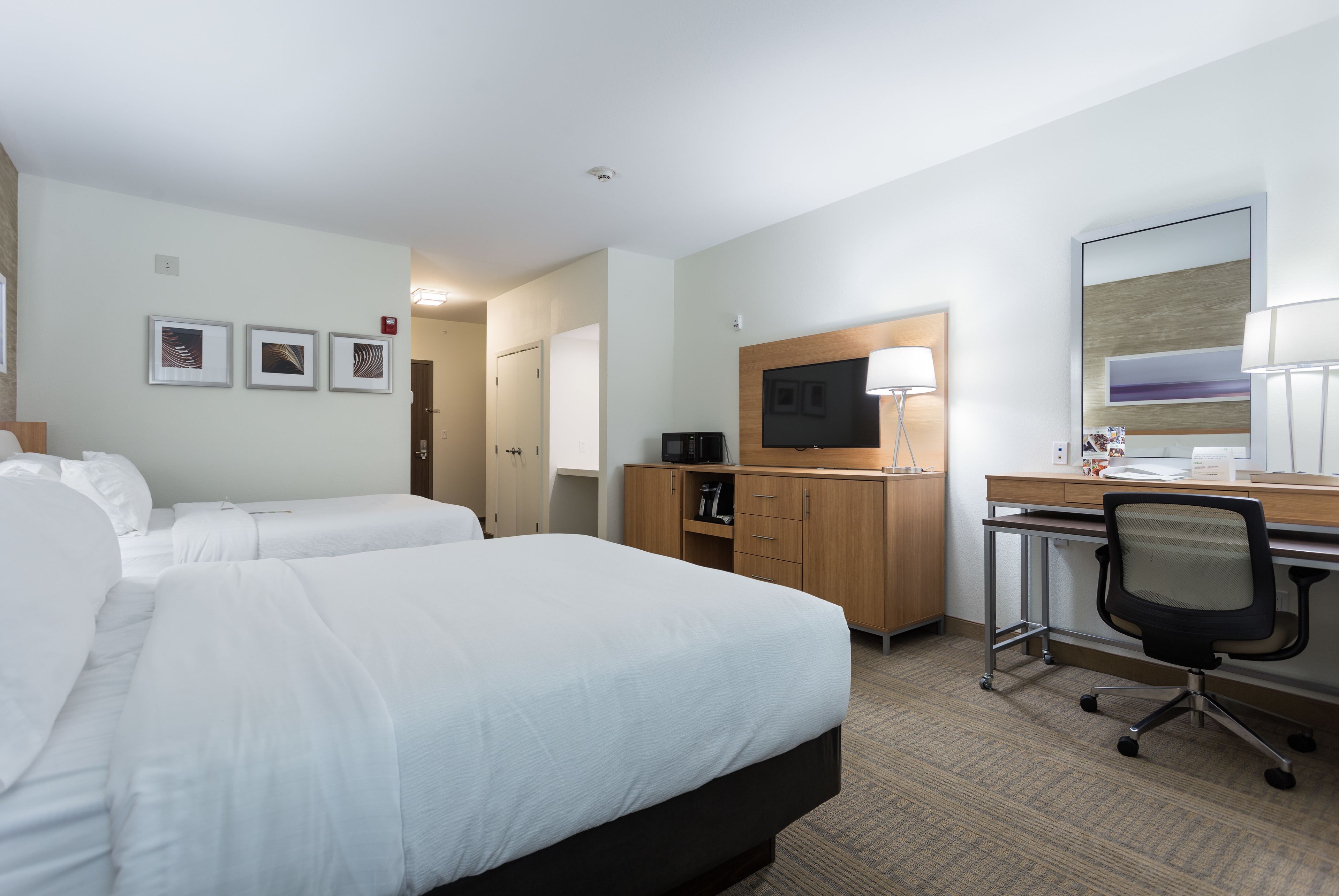Habitación de hotel con dos camas, un escritorio con computadora, televisión y armario.