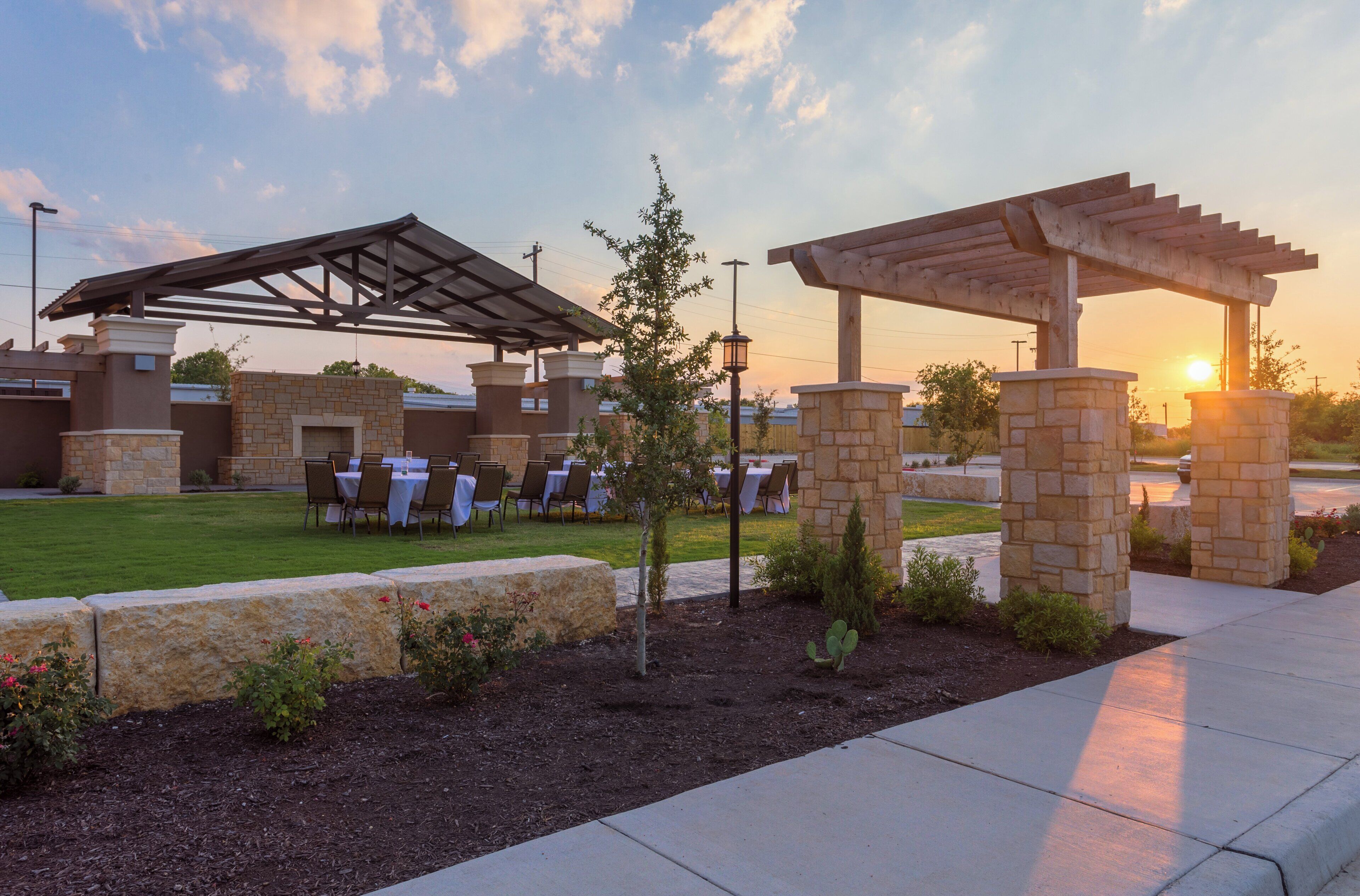 An outdoor patio with tables and chairs, a pergola, and stone pillars.