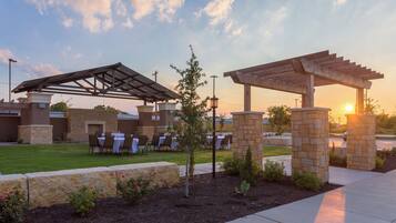 An outdoor patio with tables and chairs, a pergola, and stone pillars.