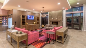 A modern hotel lobby with a wooden reception desk, a television, comfortable seating, and a fireplace. - Holiday Inn San Marcos-Convention CTR Area by IHG (San Marcos)