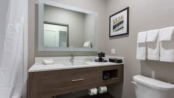 A modern bathroom with a white sink, wooden vanity, and a large mirror. There is a framed picture on the wall and a toilet with a white tank.
