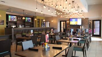 A restaurant with multiple tables and chairs, a bar area with a television, and a sports game displayed on a screen.