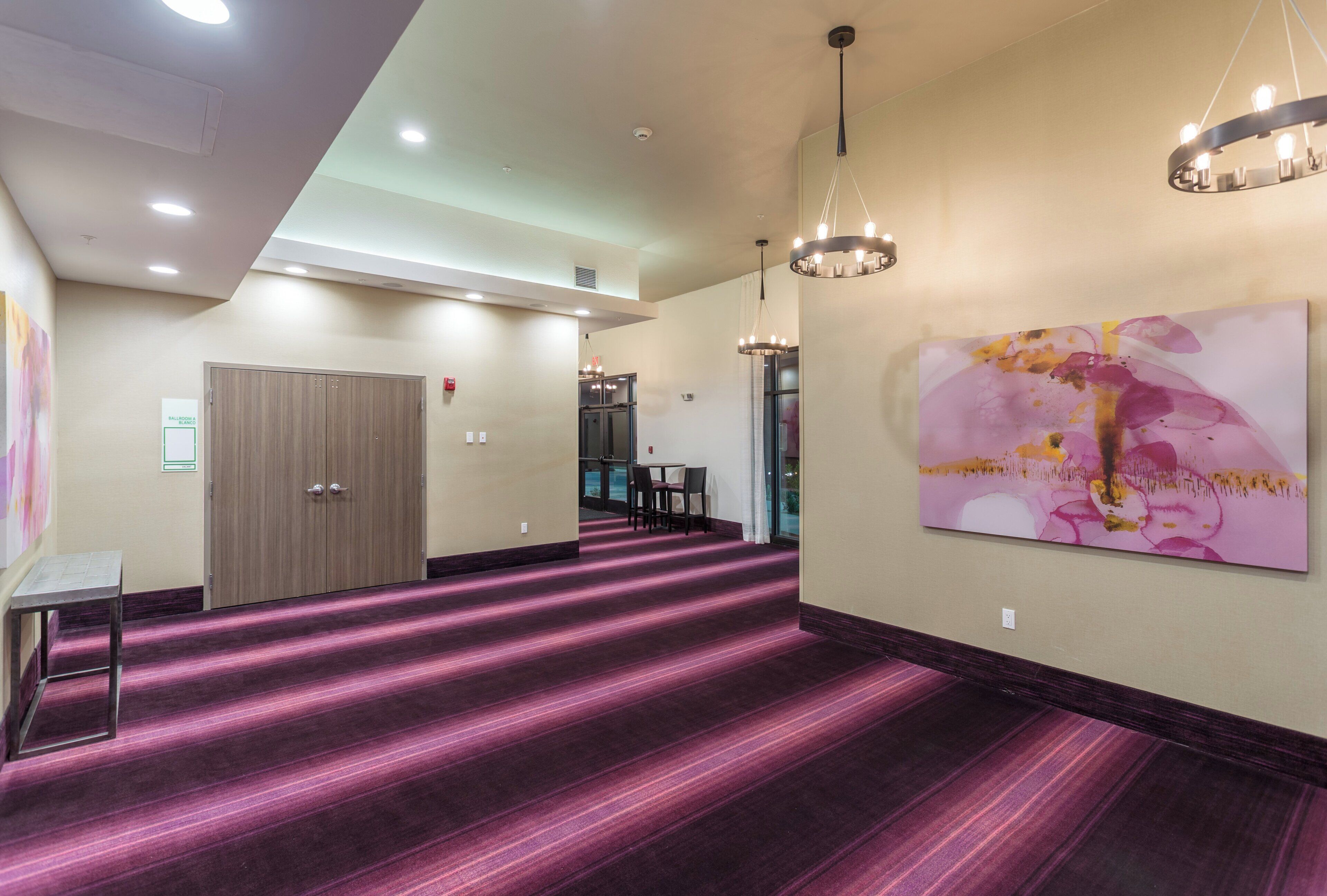 Un couloir d’hôtel avec un tapis violet, une porte, une table et un tableau accroché au mur.