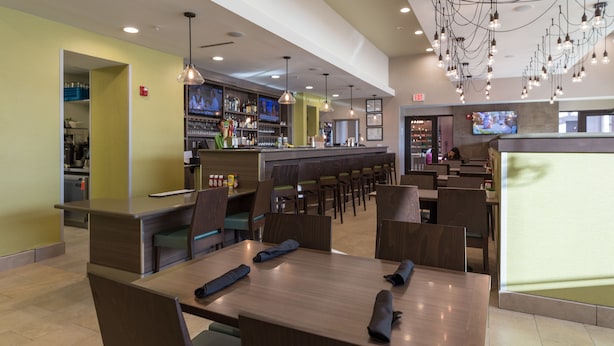 A restaurant with multiple tables and chairs, a bar area with shelves of bottles, and hanging light fixtures. - Holiday Inn San Marcos-Convention CTR Area by IHG (San Marcos)