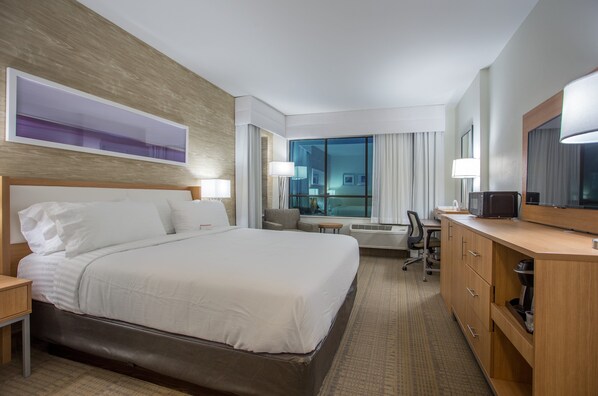 Hotelkamer met een groot bed, een bureau met een computer, een stoel en een raam met gordijnen.