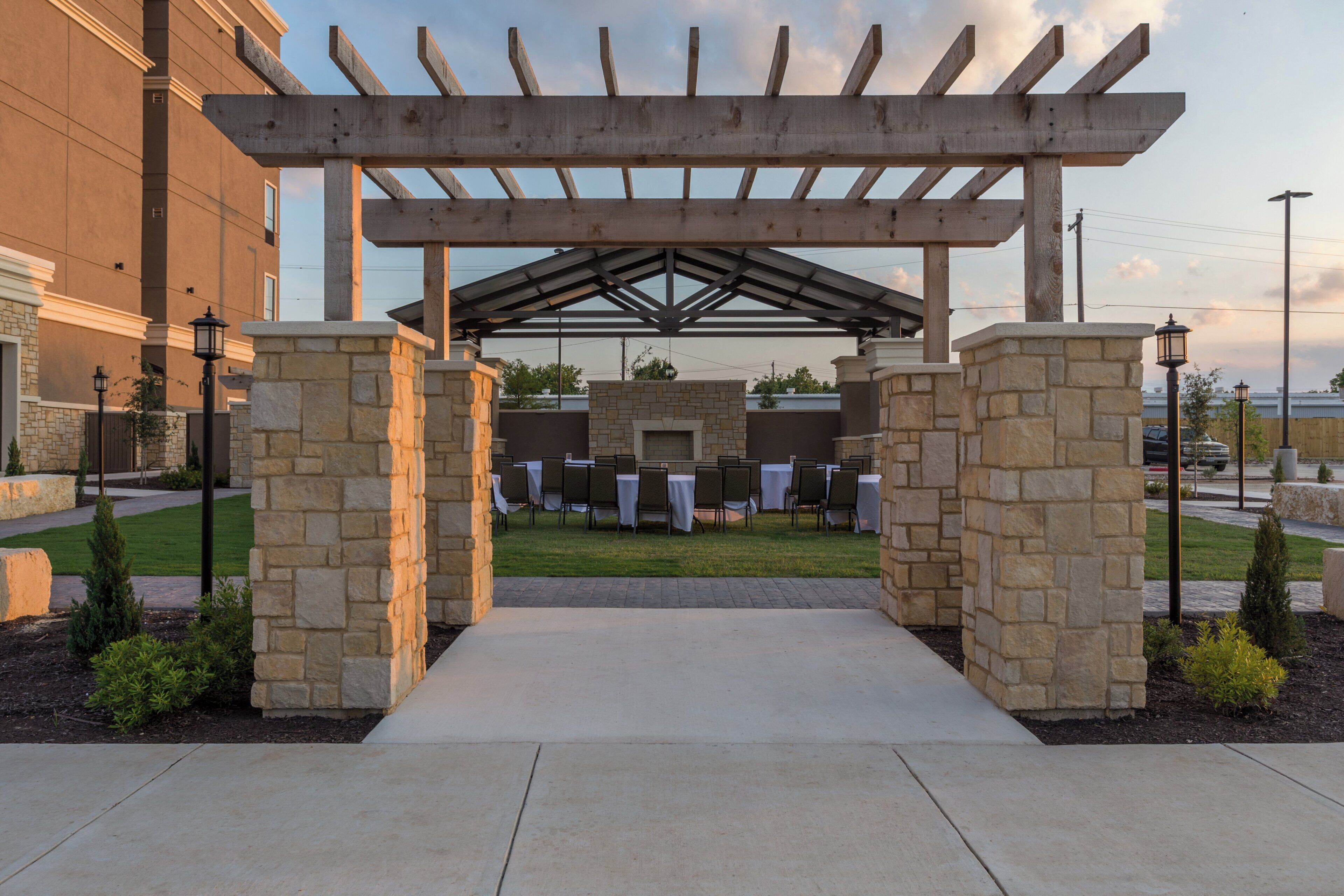 A covered outdoor seating area with stone pillars and tables, leading to a building entrance.