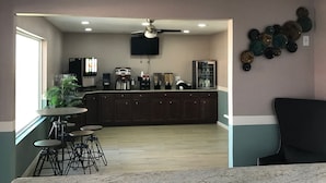 Uma cozinha moderna com uma ilha central, banquetas, máquina de café e televisão de tela plana.