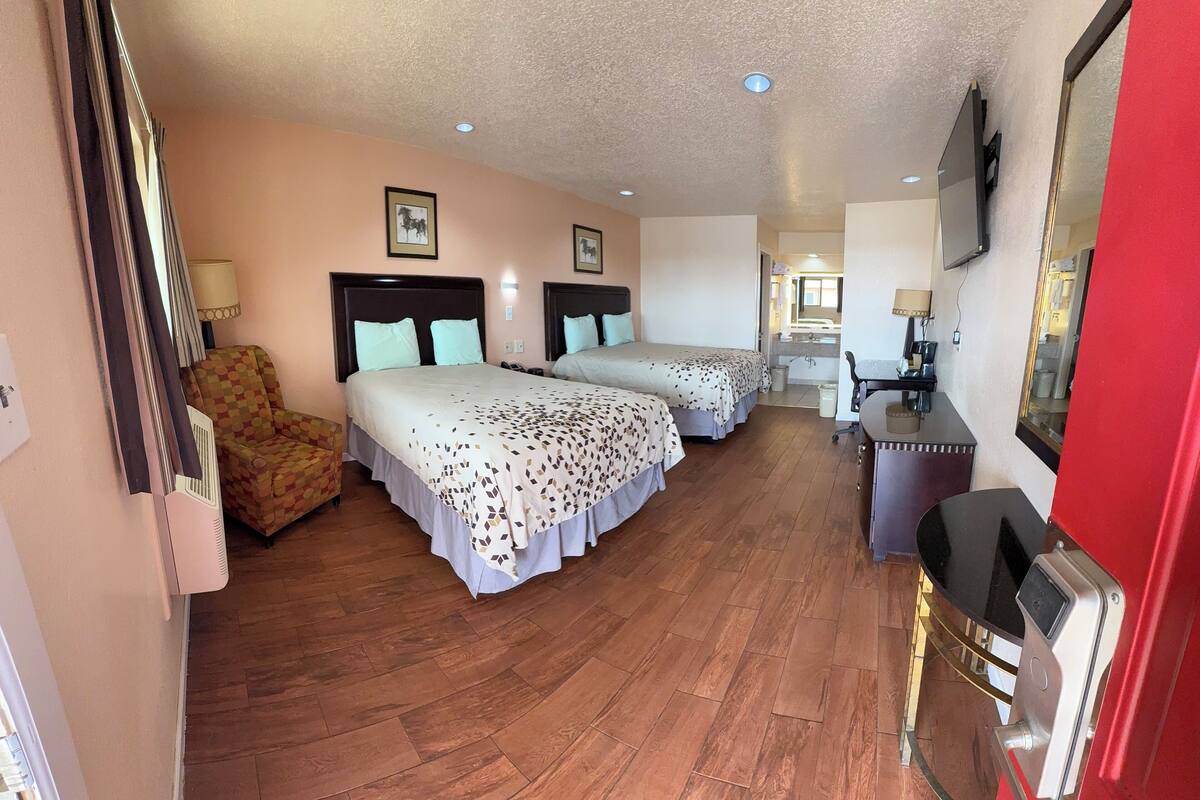 A hotel room with two beds, a desk, a chair, a TV, and a bathroom visible in the background.