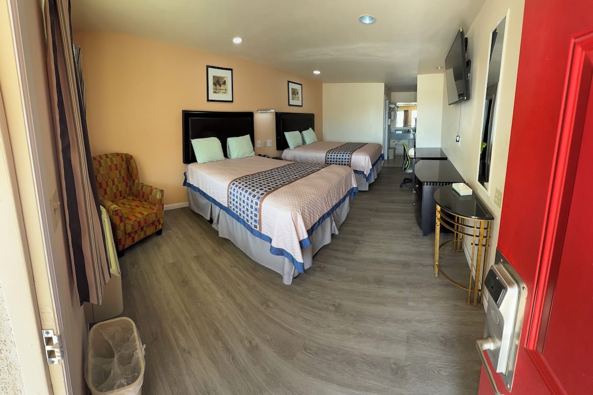 A hotel room with two beds, a desk, a chair, and a trash bin.