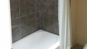 A bathroom with a shower enclosure, dark tiled walls, and a white bathtub.