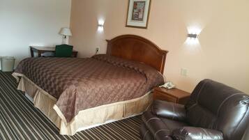 A hotel room with a large bed, a leather armchair, a desk with a lamp, and a telephone on the nightstand.