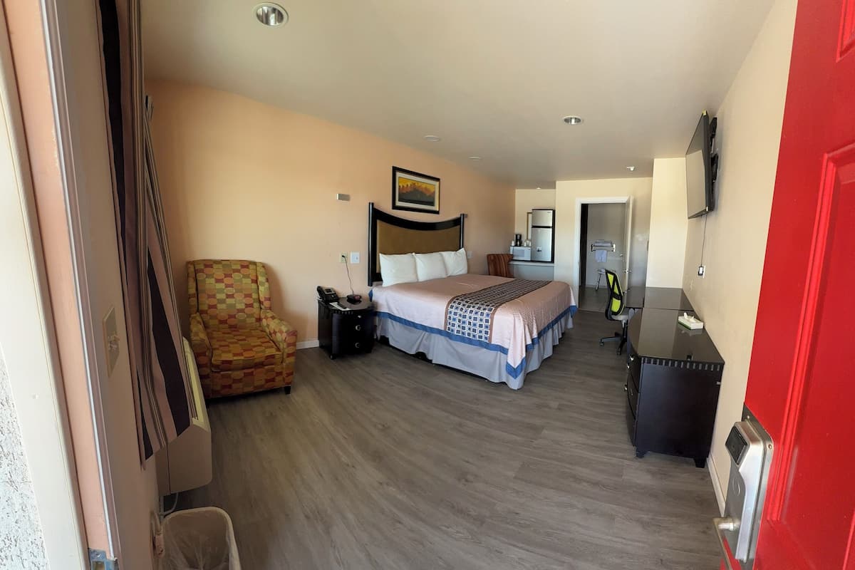 A hotel room with a bed, a chair, a desk, and a trash bin.