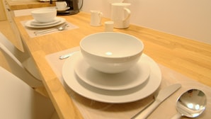 A neatly arranged dining area with white ceramic bowls, plates, and a coffee maker on a wooden table. - IRS ROYAL APARTMENTS - IRS Cztery Oceany (Gdansk)