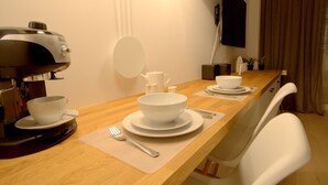 A dining table set with white plates, bowls, and cutlery, a coffee maker, a kettle, and a small potted plant. - IRS ROYAL APARTMENTS - IRS Cztery Oceany (Gdansk)