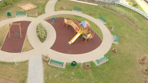 An aerial view of a playground with a slide, swings, and a circular walking path. - IRS ROYAL APARTMENTS - IRS Cztery Oceany (Gdansk)