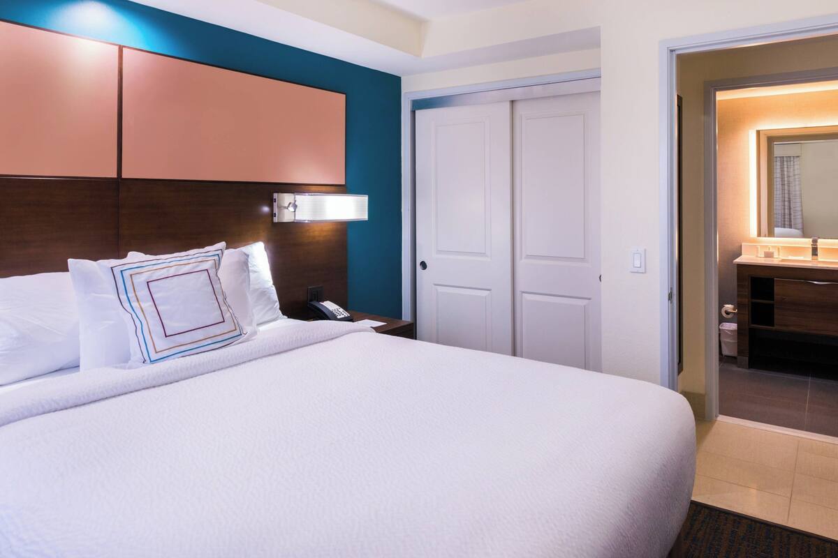 A hotel room with a large bed, a bedside table with a phone, a wall-mounted light, and a door leading to a bathroom.