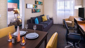 Une chambre d’hôtel comprenant un lit, un canapé, une table à manger dressée avec des assiettes et des verres, une télévision et des œuvres d’art accrochées au mur.