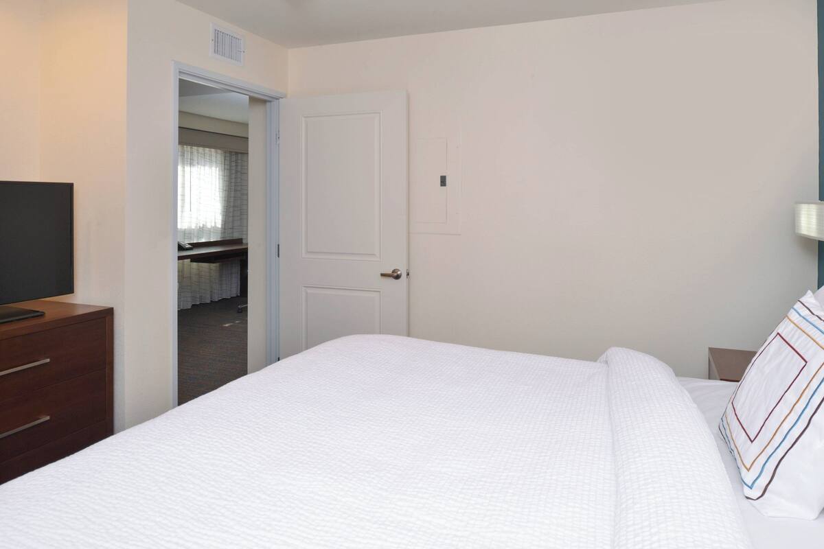 A hotel room with a bed, a dresser, a television, and a door leading to a bathroom.