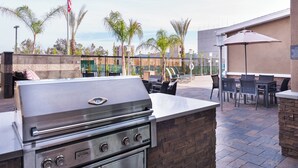 Une cuisine extérieure dotée d’un barbecue en acier inoxydable, située à côté d’un espace détente avec des tables et des chaises.