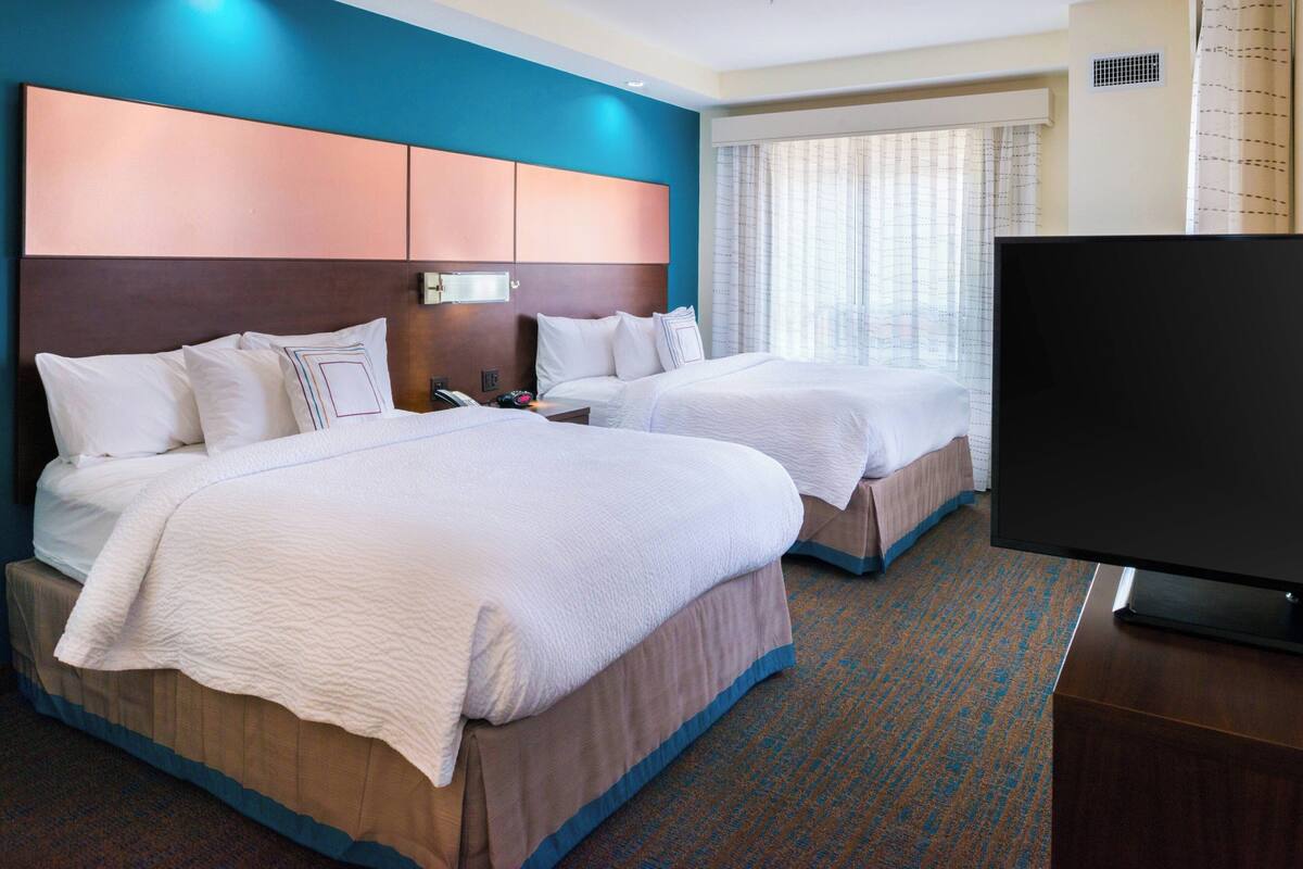 A hotel room with two beds, a flat-screen TV, and a window with curtains.