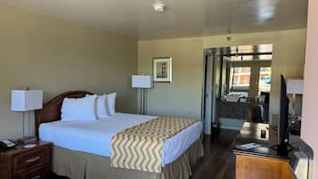 A hotel room with a bed, bedside lamps, a desk with a computer, a mirror, and a bathroom visible through an open door.