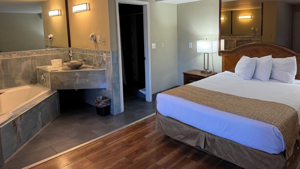 A hotel room with a bathroom, a bed, a nightstand, and a mirror. - Travelodge by Wyndham Reno Downtown (Reno)