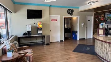 A hotel lobby with a reception desk, seating area, and a kitchenette.