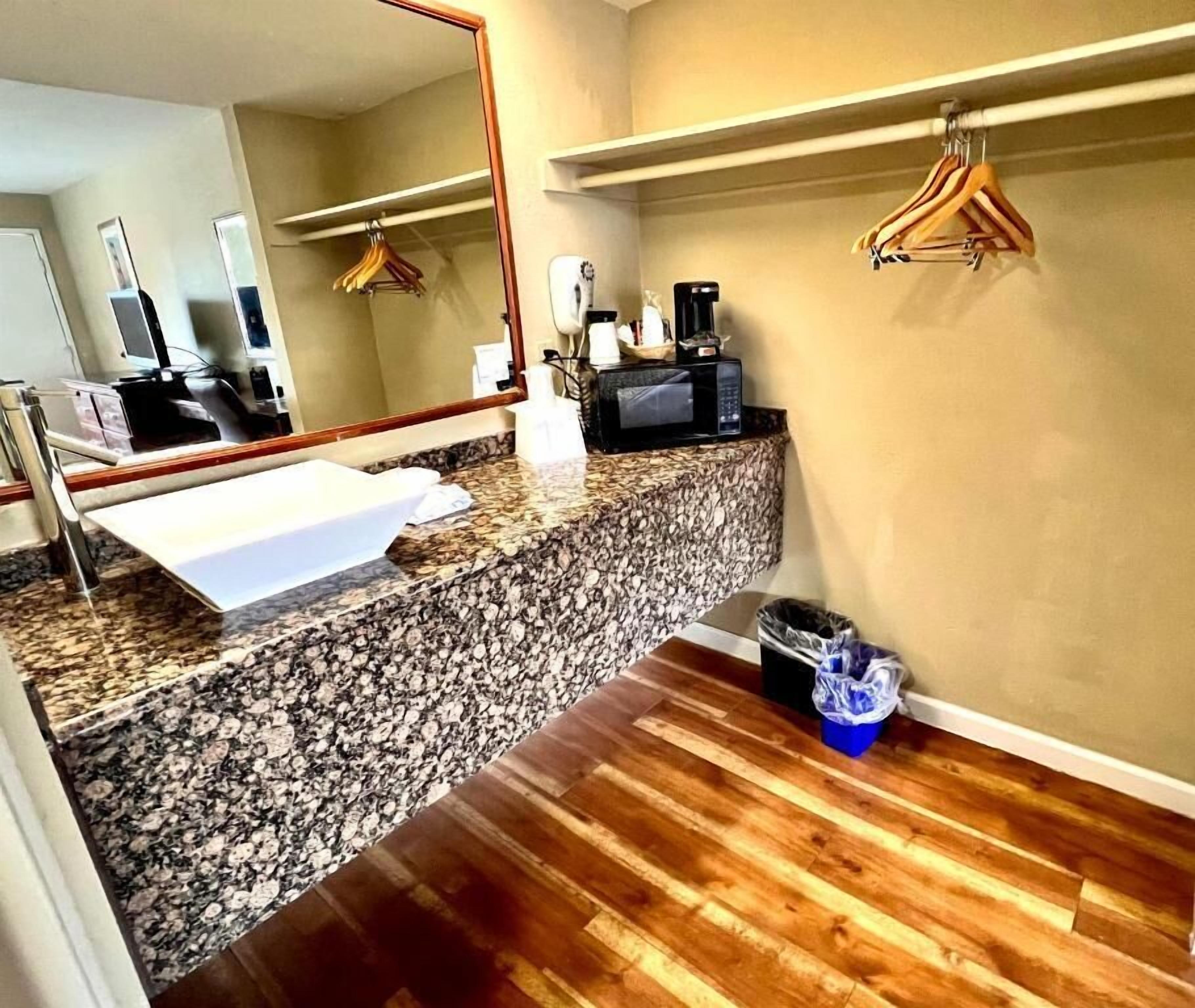 Un baño con encimera de granito, lavamanos, espejo, cafetera y un cubo de basura.