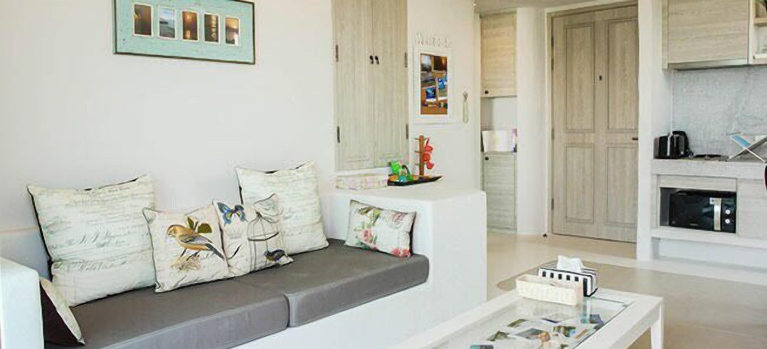 A modern living room with a grey sofa, a coffee table, and a kitchen area with cabinets and a microwave.