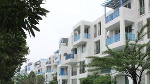 A modern residential building with multiple balconies, a landscaped garden, and a pool area. - Chelona Khaotao Hua Hin E702 (Hua Hin)