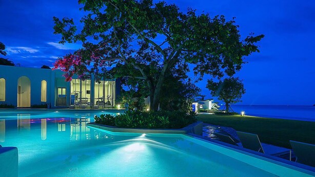 A pool area with a view of the ocean, a tree, and a building with arched windows. - Chelona Khaotao Hua Hin E702 (Hua Hin)
