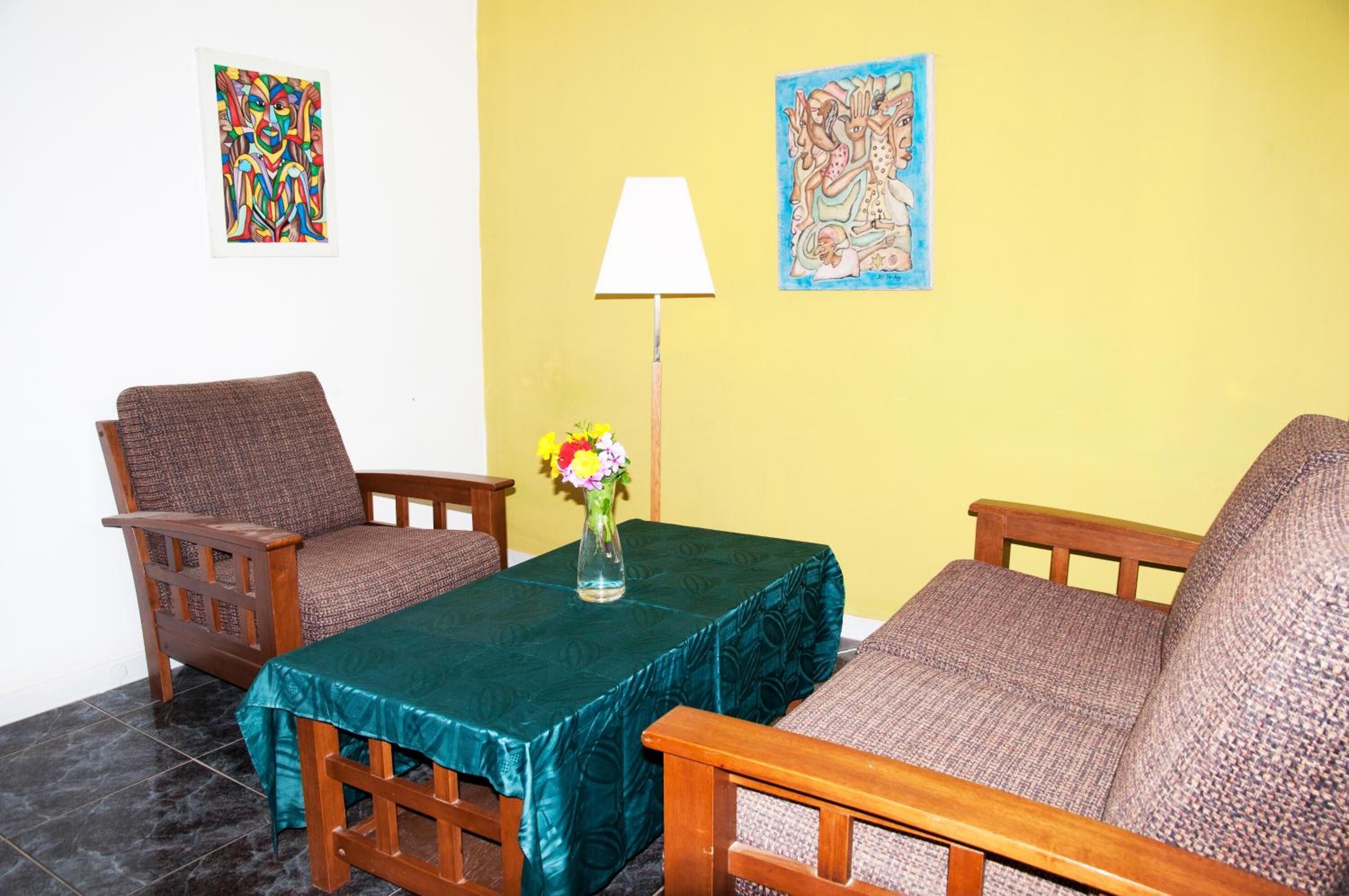Ein Zimmer mit einem türkisblauen Tisch, zwei Holzstühlen, einer Blumenvase, einer Lampe und zwei Wandbildern.