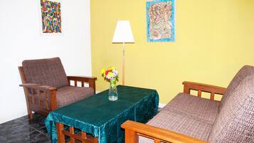 Ein Zimmer mit einem türkisblauen Tisch, zwei Holzstühlen, einer Blumenvase, einer Lampe und zwei Wandbildern.
