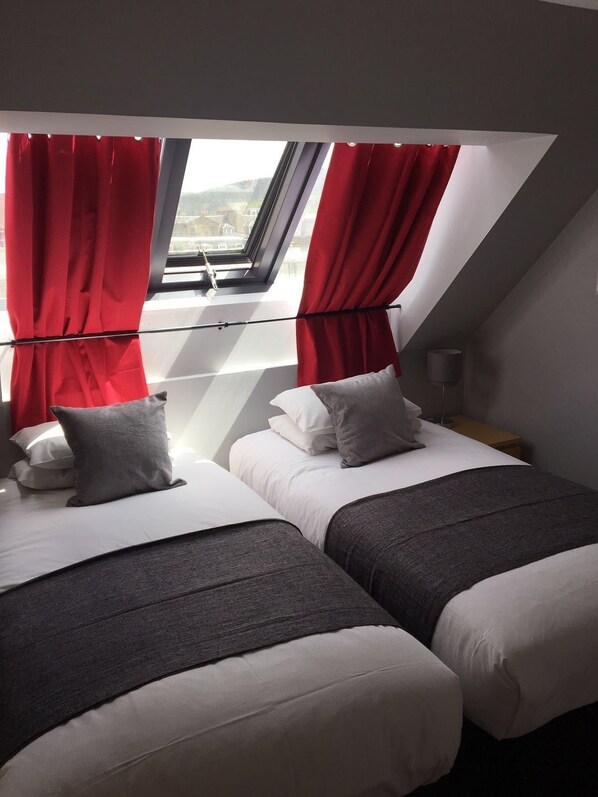 A bedroom with two beds, red curtains, a skylight, and a view of the city.