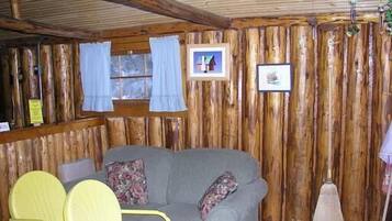 Ein rustikales Blockhaus-Interieur mit einer Holzwand, einem grauen Sofa, zwei gelben Stühlen und einem Besen.