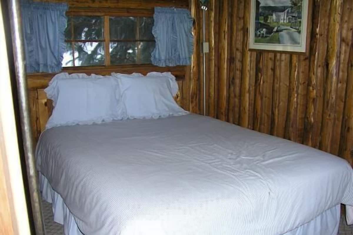 Una cama en una habitación con paredes de madera y una ventana con cortinas.