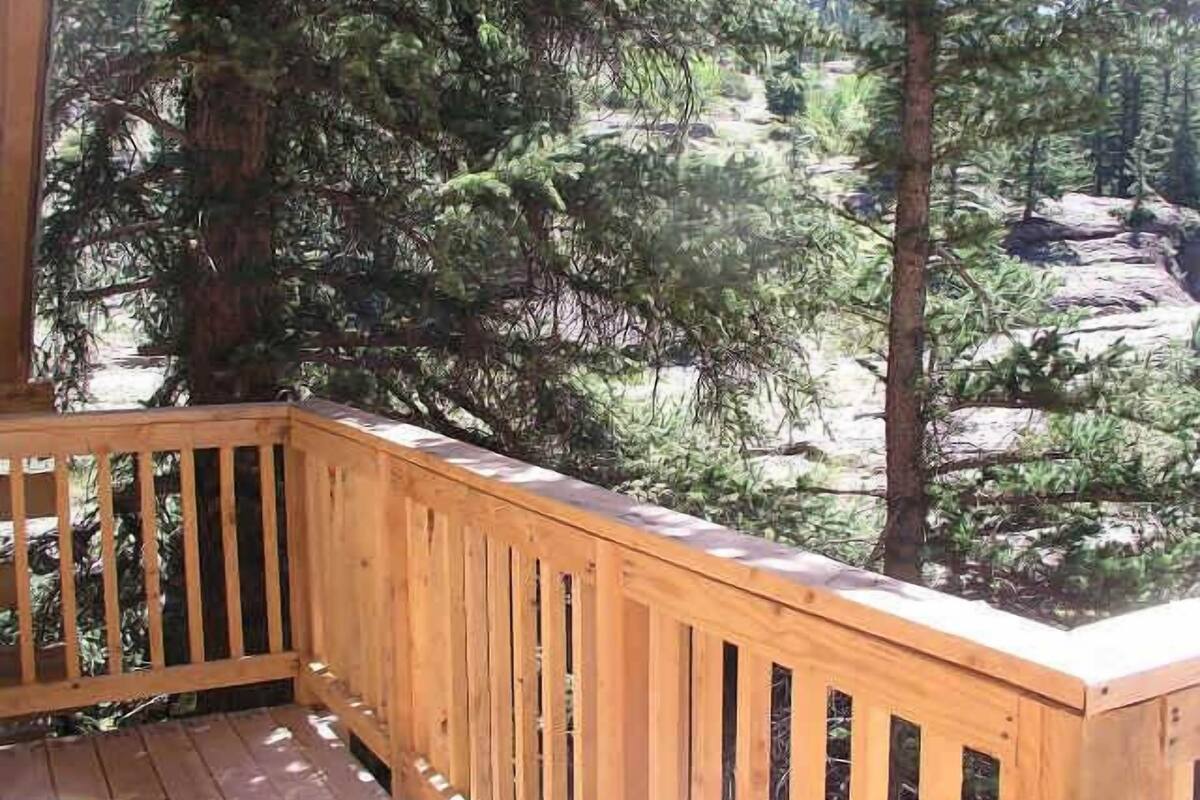 Terraza de madera con barandilla que da a un área boscosa con árboles altos.