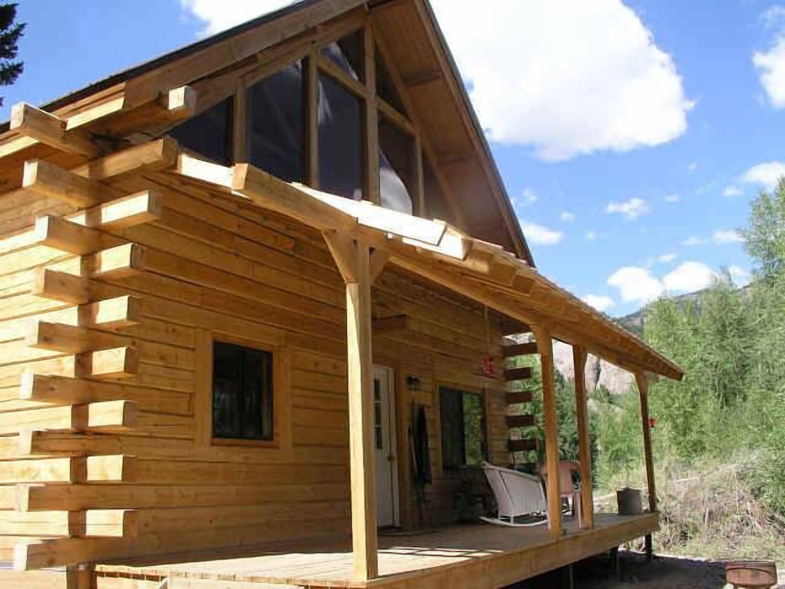 A wooden cabin with a porch, large windows, and a door.