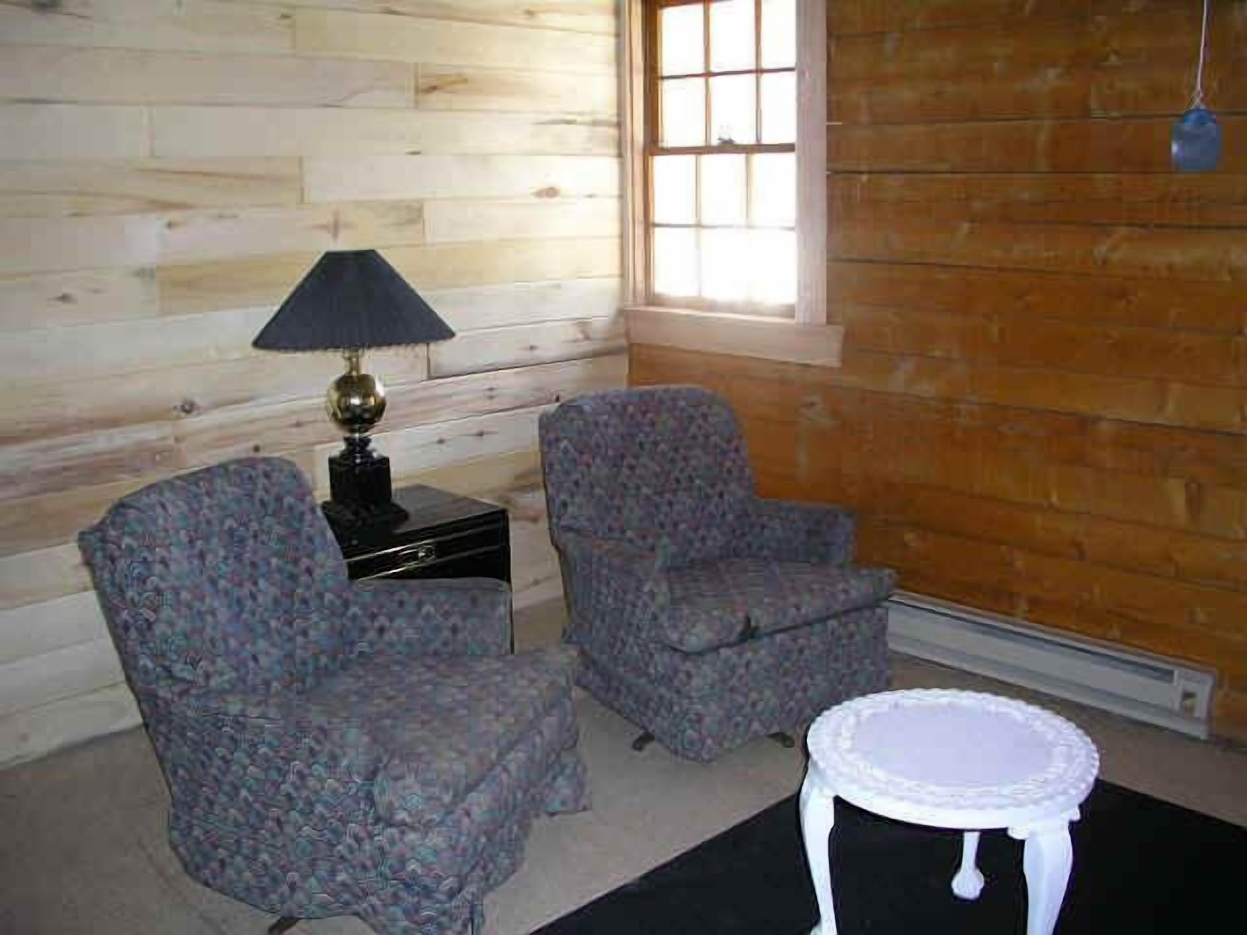Una habitación con paredes de madera, dos sillones estampados, una mesita y una lámpara.