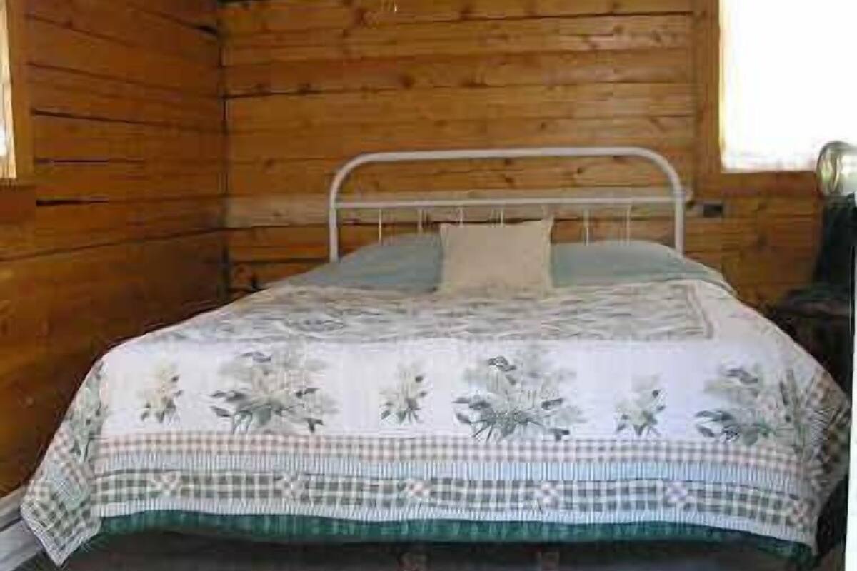 Una cama individual con estructura metálica, colcha de estampado floral y manta de cuadros.